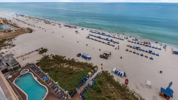 A beach with rows of sun loungers and umbrellas, a swimming pool, and a lifeguard tower.