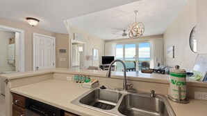 A kitchen with a double sink, a dishwasher, and a view of the ocean through large windows.