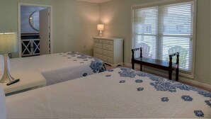 A bedroom with two beds, a dresser, a lamp, a window with blinds, and a door leading to another room. - It's Five O'clock Somewhere 6/3) (Panama City Beach)