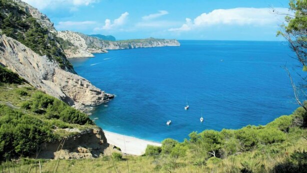 Un paysage côtier caractérisé par des falaises rocheuses, une mer bleue et limpide, et une plage de sable.