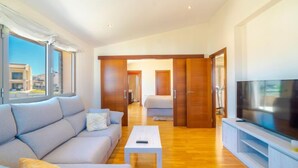 Un salon moderne avec un canapé, une table basse et un téléviseur. Le sol est en bois et il y a une vue sur l’extérieur.