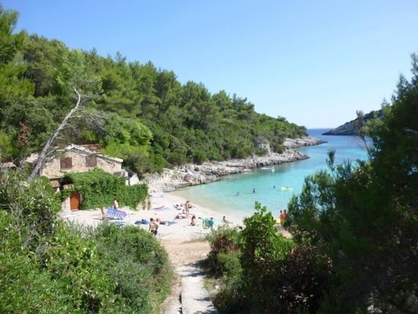 Stroll along the serene coastal path to a tranquil beach surrounded by lush greenery and rocky outcrops.