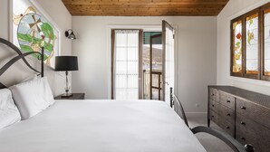Un dormitorio con cama, cómoda, lámpara, ventana con vistas y puerta que da a un espacio exterior.
