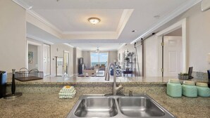 A kitchen with a double sink, granite countertop, and a view to the living area. - Ocean Ritz by iTrip Panama City Beach (Panama City Beach)