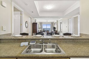 A hotel kitchen with a double sink, granite countertops, and a view of the ocean through the dining area. - Ocean Ritz by iTrip Panama City Beach (Panama City Beach)