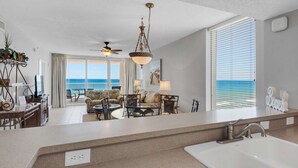 Une chambre d’hôtel moderne dotée d’un grand balcon, d’un ventilateur de plafond, d’un lustre, d’un ensemble de canapés et offrant une vue sur l’océan.