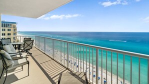 Un balcon avec vue sur l’océan et la plage, agrémenté de mobilier d’extérieur et d’une balustrade.