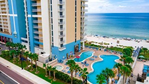 Un hôtel de grande hauteur doté de nombreux balcons, d’un espace piscine avec des chaises longues et offrant une vue sur la plage.