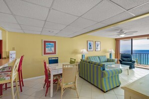 A room with a dining table, chairs, a sofa, and a balcony with a view. - Pelican Walk 904 (Panama City Beach)