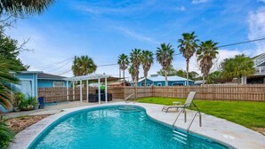 Un jardin avec une piscine, un patio couvert et une clôture en bois.