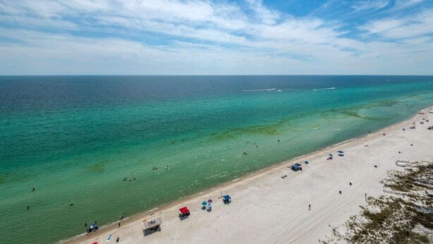 A beach with clear turquoise water, a sandy shore, and a few umbrellas and beach chairs. - Palazzo by iTrip Panama City Beach (Panama City Beach)