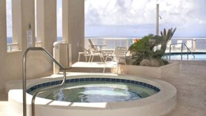 Ett poolområde med en bubbelpool, solstolar och utsikt över havet.