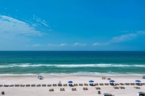 A beach with rows of sun loungers and umbrellas, a clear blue sky, and the ocean in the background. - Regency Towers 521 (Panama City Beach)