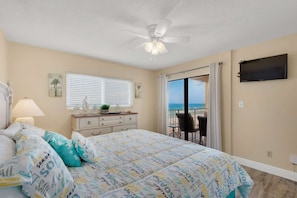 A bedroom with a bed, a dresser, a ceiling fan, a window with blinds, a TV, and a view of the beach. - Regency Towers 521 (Panama City Beach)