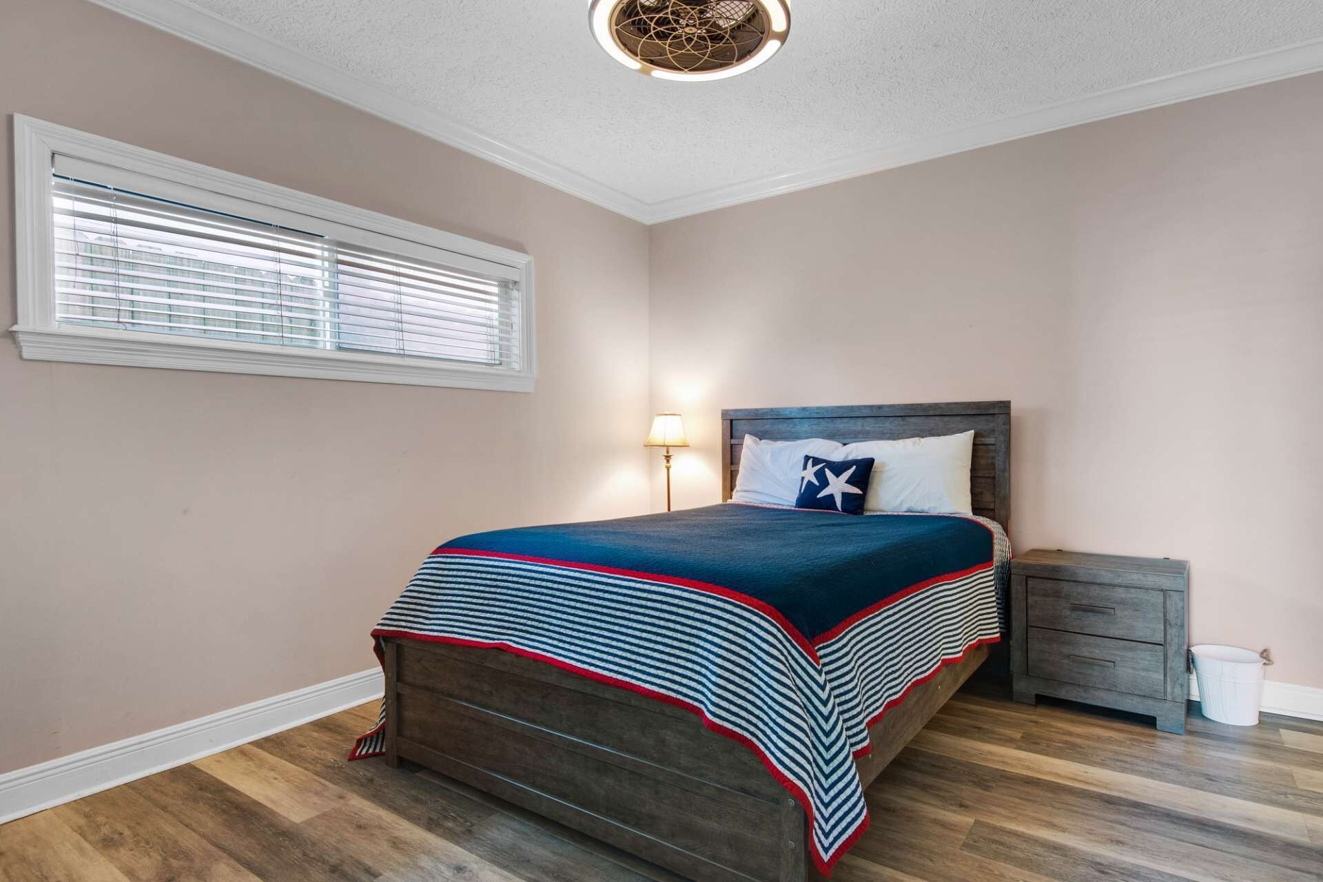A bedroom with a wooden bed, a nightstand, a lamp, and a window with blinds.