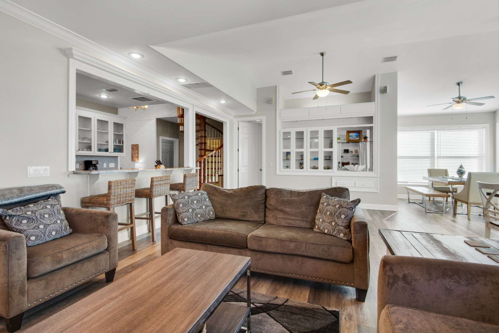 A spacious living room with a brown sofa set, a wooden coffee table, and a dining area with a wooden table and chairs.