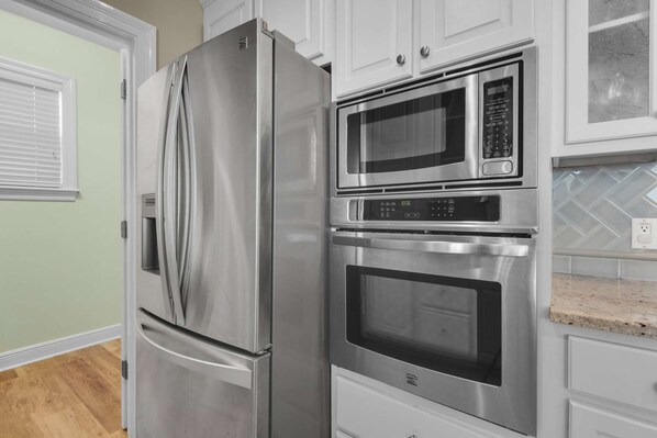Una cocina con un refrigerador de acero inoxidable, un microondas y dos hornos.