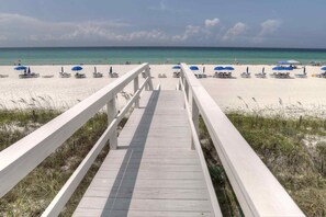 A wooden boardwalk leading to a beach with white sand and clear blue water.