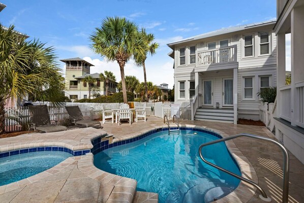 A swimming pool with a curved design, surrounded by a white fence, and adjacent to a building with a balcony.