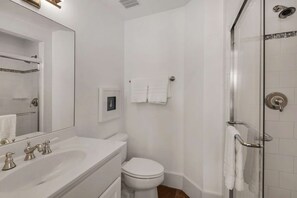 A modern bathroom with a white sink, vanity, and toilet. There is a glass shower enclosure and a framed picture on the wall.