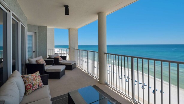 A balcony with a view of the beach, a sofa, and a glass table. - Long Beach Resort by iTrip Panama City Beach (Panama City Beach)