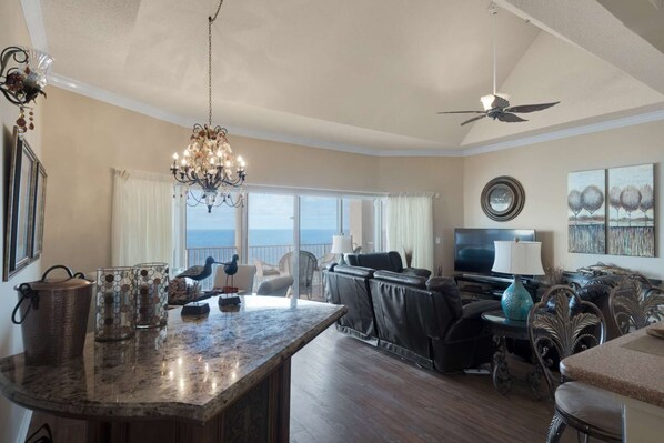 A spacious living room with a large window, a chandelier, a ceiling fan, and a television.