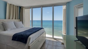 A bedroom with a bed, a TV, and a large window overlooking the sea. - Long Beach Resort by iTrip Panama City Beach (Panama City Beach)