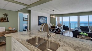 A kitchen with a large island, a dining area with a view of the ocean, and a balcony with a view of the ocean. - Long Beach Resort by iTrip Panama City Beach (Panama City Beach)