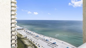 A beachfront hotel with multiple balconies, a sandy beach with umbrellas, and the ocean in the background. - Long Beach Resort by iTrip Panama City Beach (Panama City Beach)