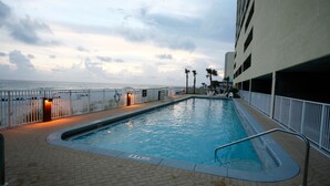Une piscine avec vue sur l’océan, une clôture blanche et un immeuble à plusieurs étages.