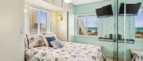 A bedroom with a bed, a ceiling fan, a TV, and a view of the beach.