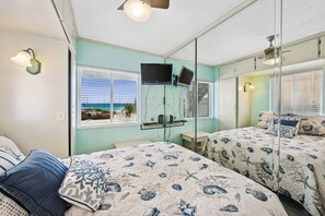 Un dormitorio con dos camas, televisión y vista al océano a través de la ventana.