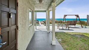 Un espacio al aire libre techado, con piso de concreto, un columpio de madera y vista al océano.