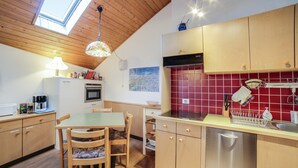 Une cuisine avec des meubles de rangement en bois, une table à manger, des chaises, un lave-vaisselle et une lucarne.