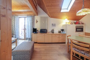 Una habitación acogedora con sofá, una mesa de comedor con sillas, una zona de cocina con electrodomésticos y un tragaluz.