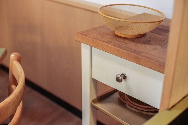 Een keukenhoek met een houten tafel, een wit kastje met een lade en een stoel.