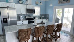 Una cocina con una isla central, taburetes de bar, un refrigerador, un microondas y un lavaplatos.