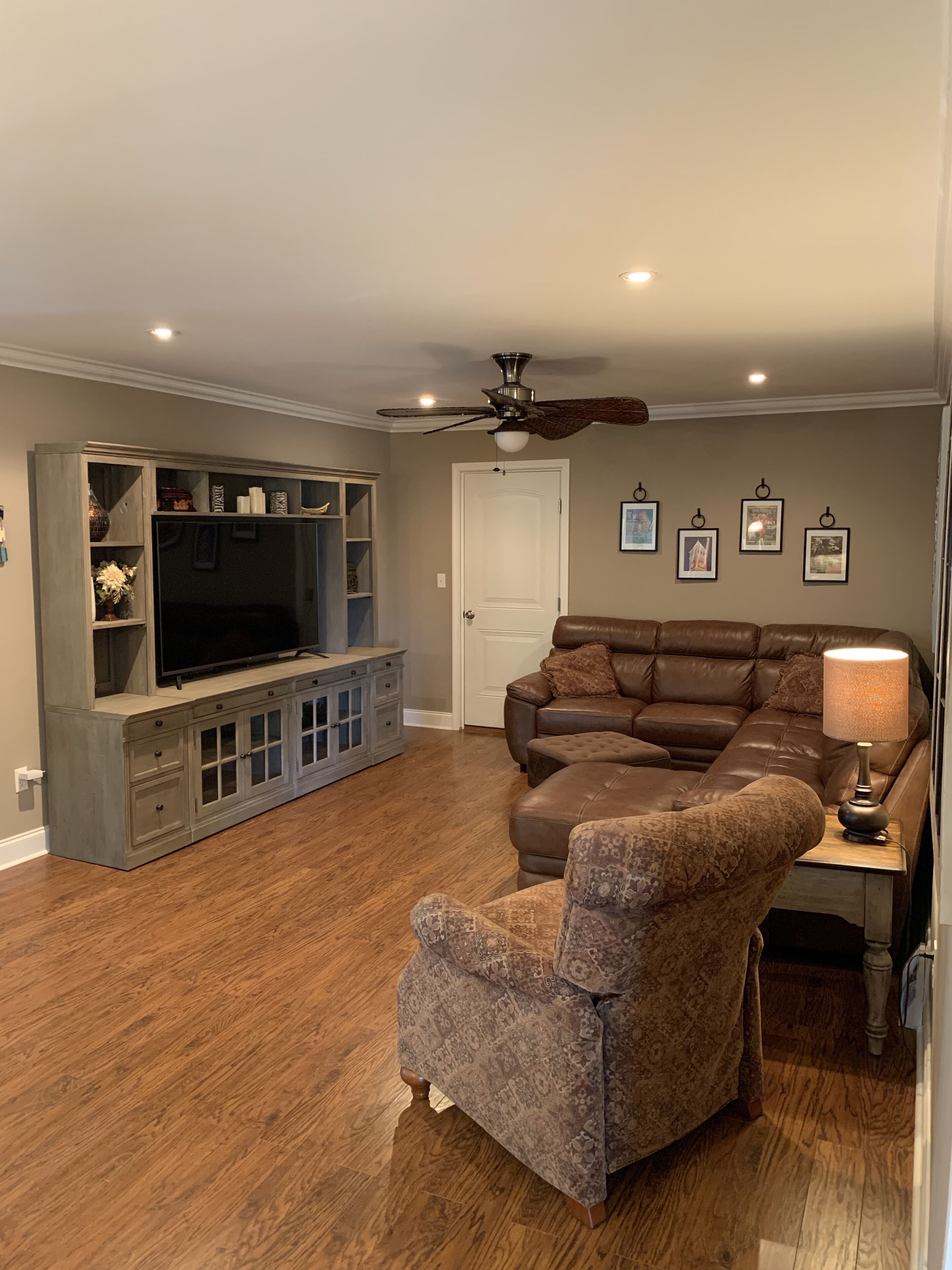A living room with a sectional sofa, a television on a cabinet, a ceiling fan, and framed pictures on the wall.