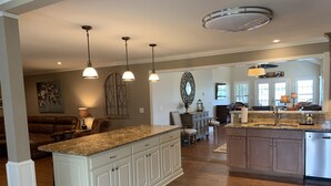 A spacious kitchen with a large island, pendant lighting, and a view into the living area. - THE Premier Clemson /Seneca Lake Home  (Seneca)