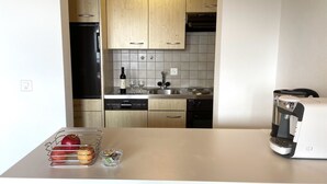 A modern kitchen with wooden cabinets, a dishwasher, a wine bottle, and a coffee machine.