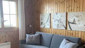 A room with a grey sofa, a white radiator, wooden panel walls, and three floral artwork pieces.