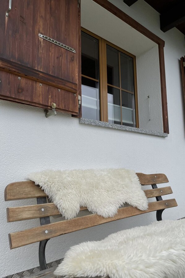A wooden bench with a white furry throw blanket, a wooden cabinet, and a window with a view of the interior.