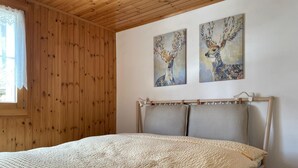 A bedroom with a wooden ceiling, a bed with a textured blanket, and two wall paintings of deer.