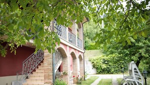Un bâtiment doté d’un escalier menant à un balcon, entouré de verdure et bordé d’un sentier.