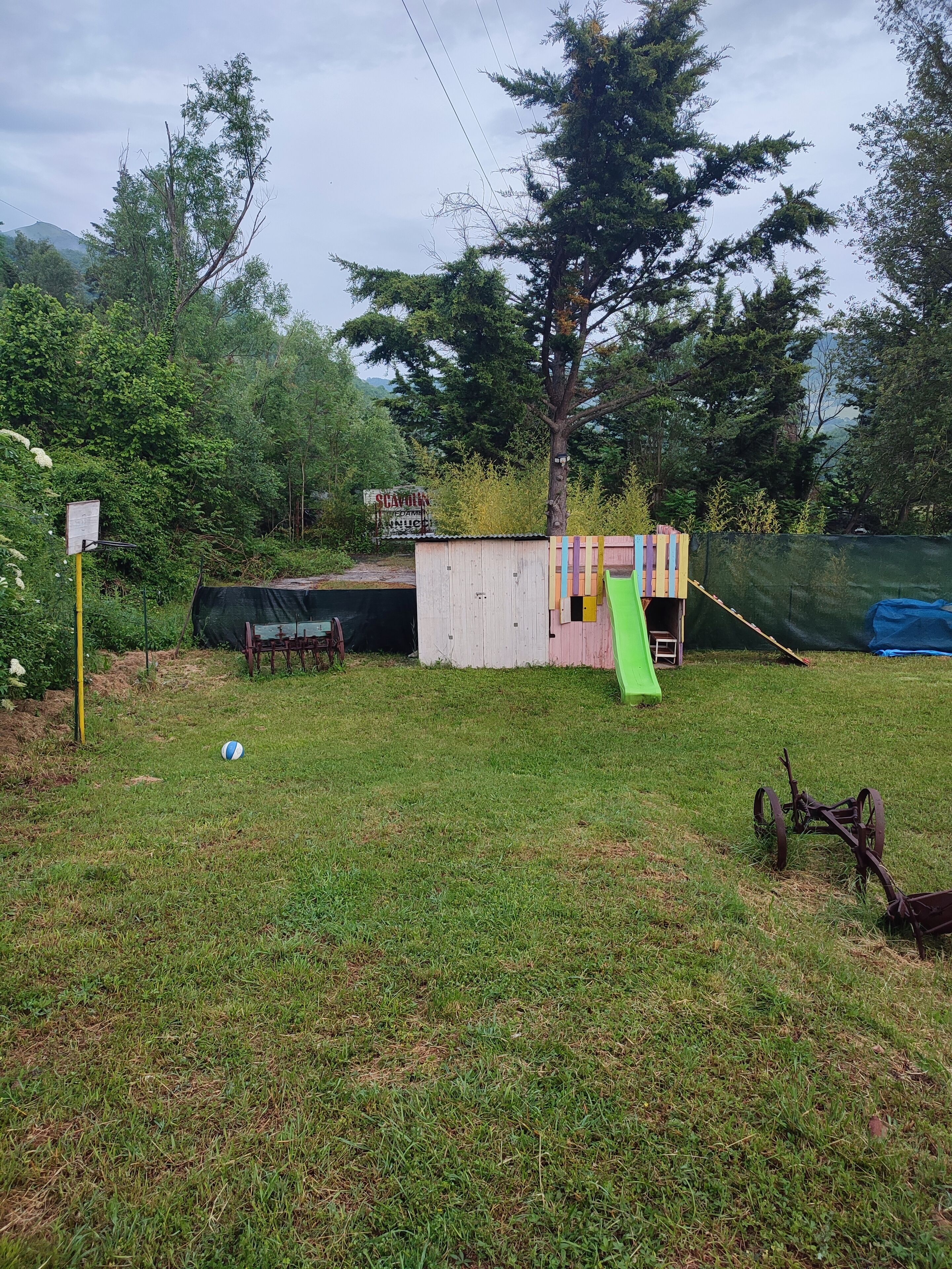A grassy outdoor area with a small shed, a green slide, and a rusty piece of machinery.