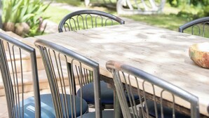 Un espace de restauration en plein air, avec des chaises en métal et une table en bois, entouré d’une végétation luxuriante et agrémenté d’une sculpture en métal blanc.