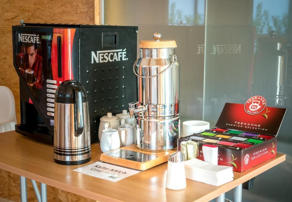 Una estación de café con una máquina de café Nescafé, una caja de selección premium Teekanne y una cafetera Keurig.