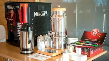 Una estación de café con una máquina de café Nescafé, una caja de selección premium Teekanne y una cafetera Keurig.