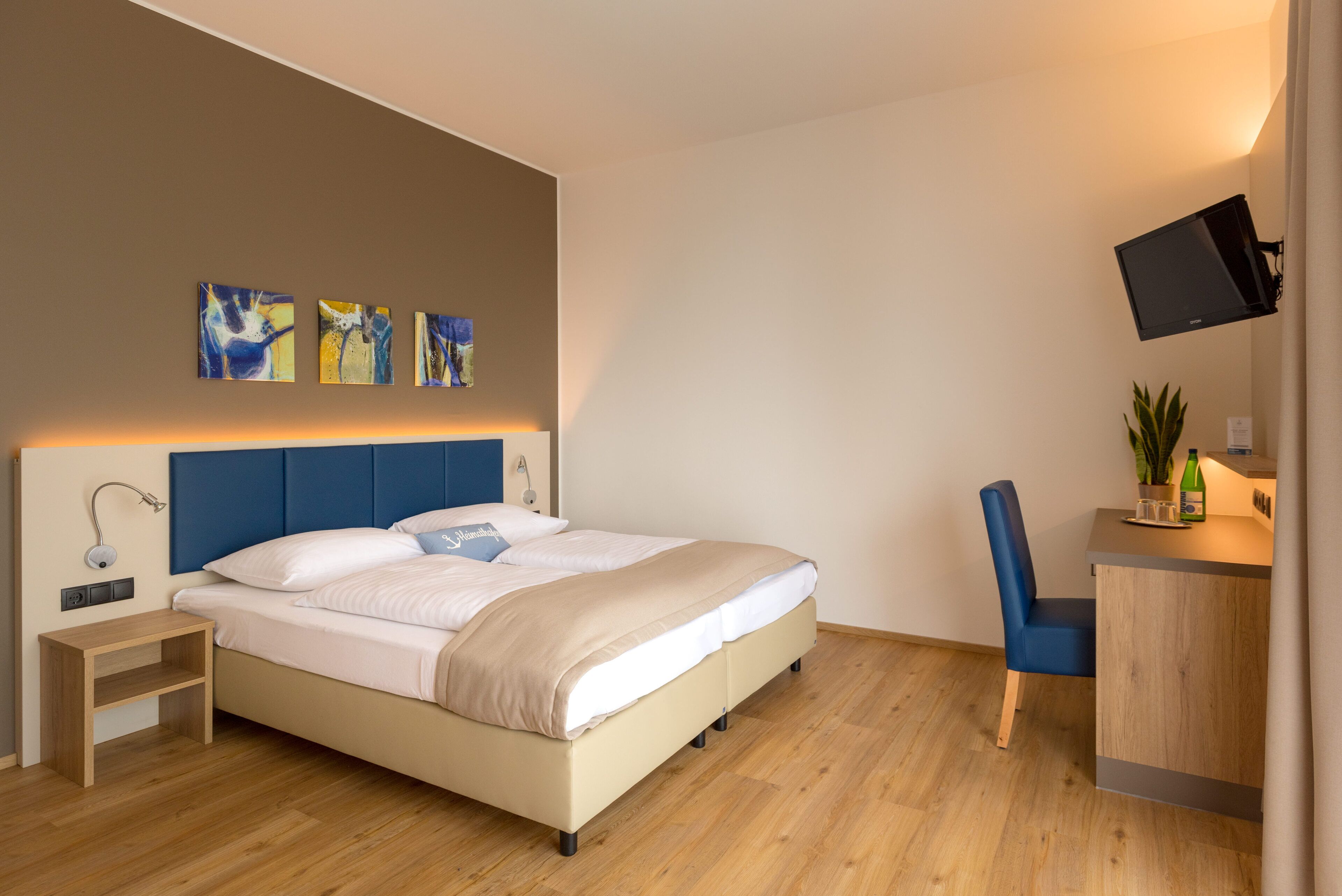 Une chambre à coucher moderne, avec un lit, une table de chevet, une chaise, un bureau et une œuvre d’art accrochée au mur.