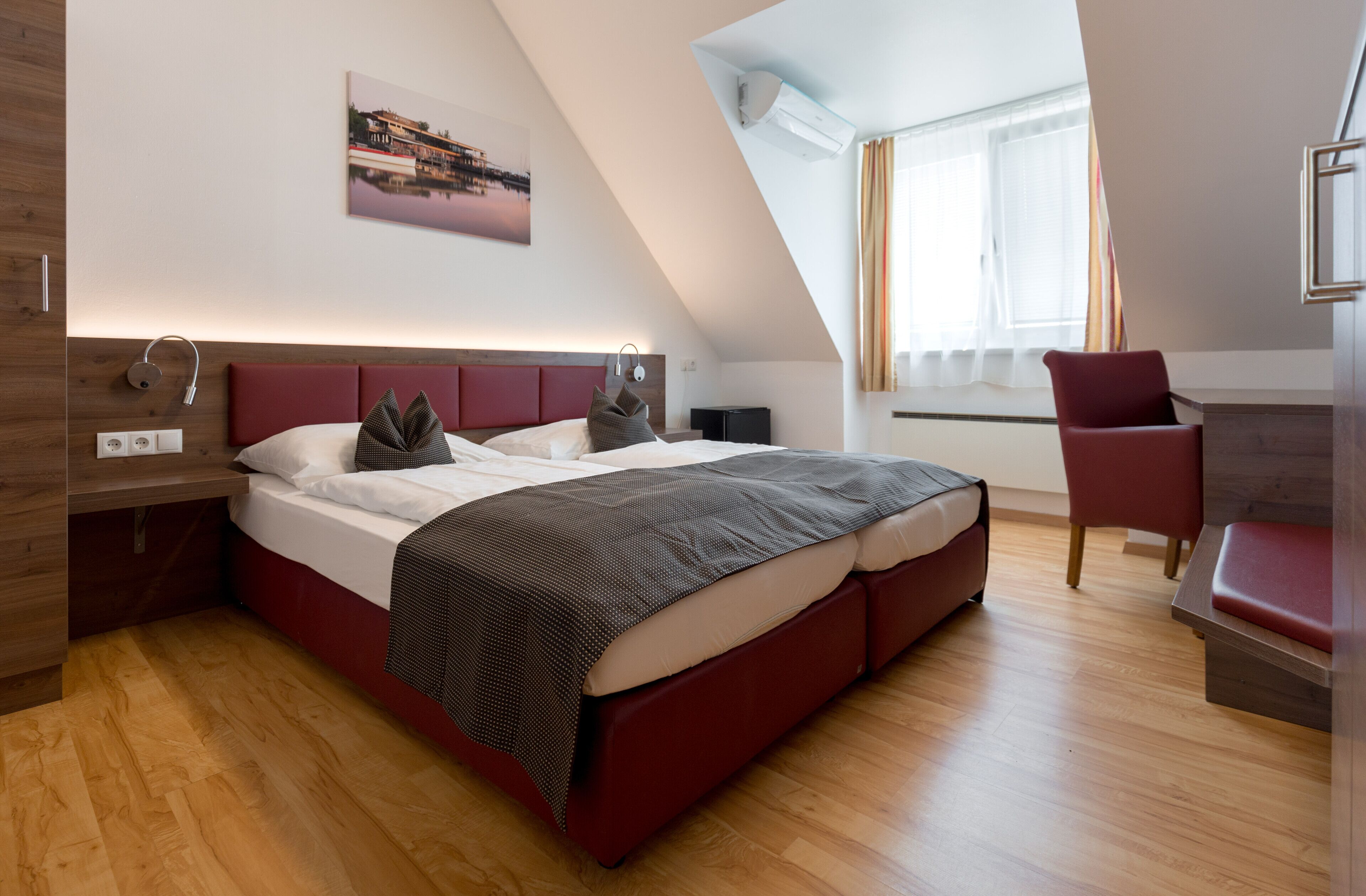 A modern bedroom with a large bed, a red chair, and a view of the outdoors through a window.